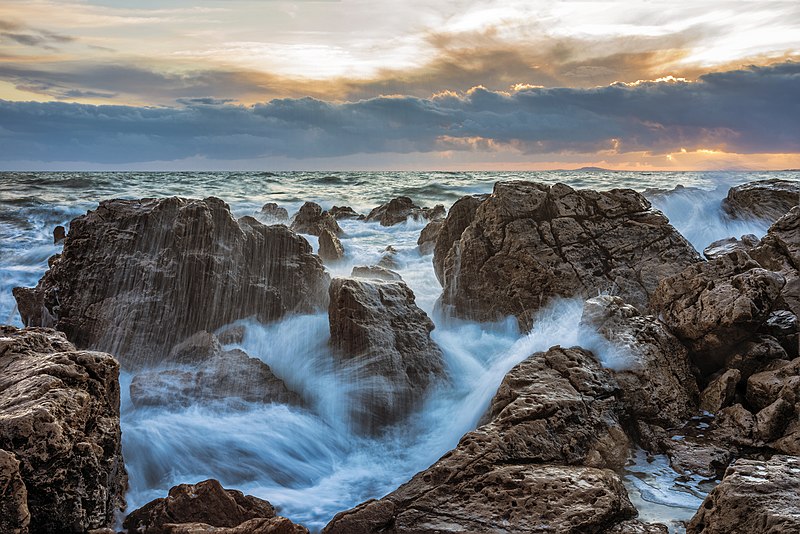 Waves gently break over rocks on the beach under a beautiful sunset.